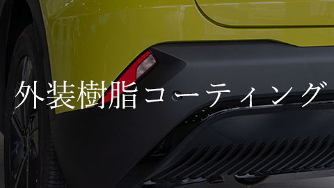 Close-up of a yellow car bumper with white Japanese overlay text reading '外装樹脂コーティング' (exterior resin coating).