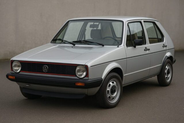 初代フォルクスワーゲン・ゴルフ（Mk1）正面3/4ビュー。シルバーメタリックの車体に特徴的な丸型ヘッドライトとシンプルなデザインが際立つ。