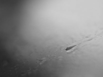 Monochrome close-up of a water droplet creating ripples on a calm surface, grayscale tones.