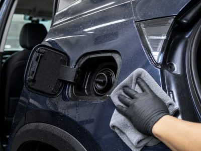 施工ブースで車の給油口とドア内側をマイクロファイバーで丁寧に拭き上げるコーティング車メンテナンスのイメージ