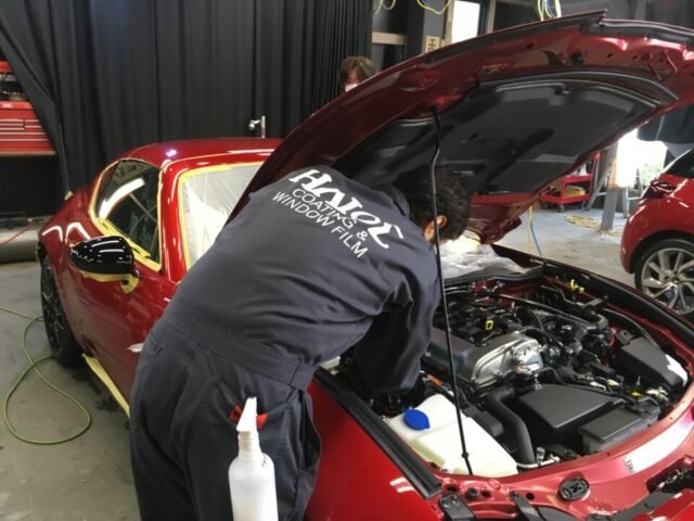 Mechanic leaning over the open hood of a red sports car in a workshop, inspecting the engine.