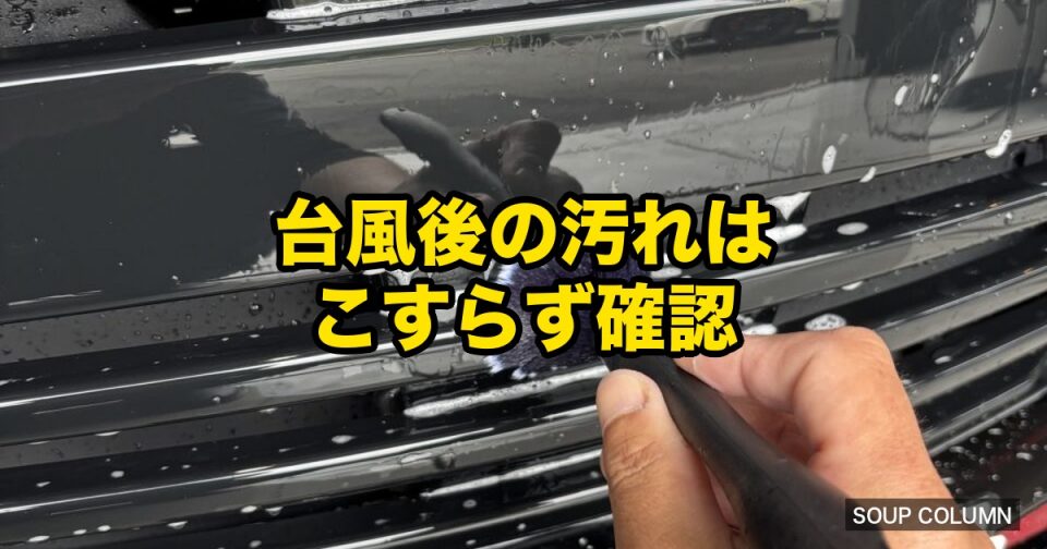Person wipes a car's front grille with a cloth; yellow Japanese tip overlay says '台風後の汚れはこすらず確認' ('After a typhoon, check dirt without rubbing').